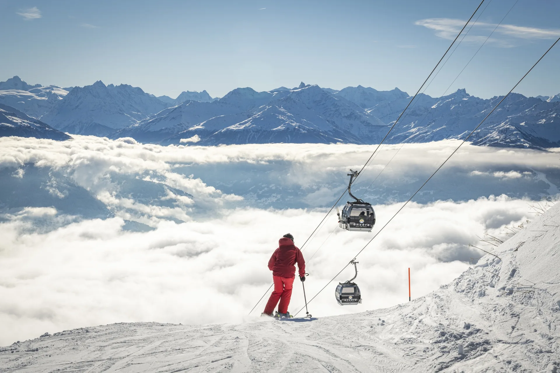 A skier above a sea of clouds in the Swiss Alps, gondolas passing overhead